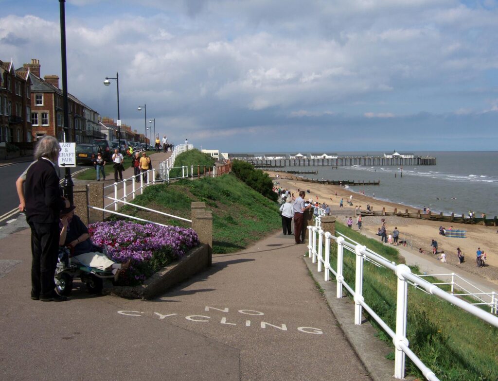 view downhill towards seaside, beach huts and pier, family group on the left