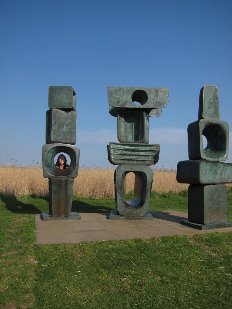 face looking through a hole in metal sculpture with reedbeds behind