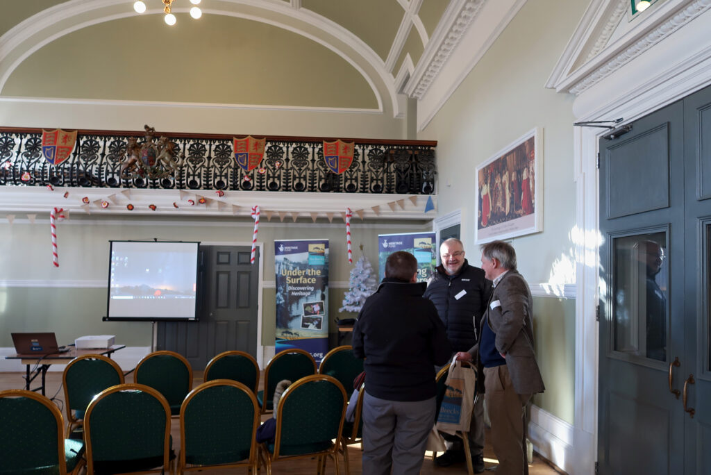 three people having a discussion in Thetford Guildhall, ornate heraldic balcony, chairs set up ready for PowerPoint presentations