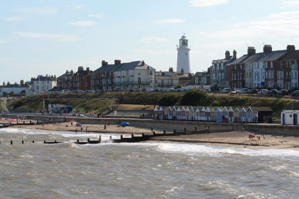 waves, beach, promenade, beach huts, with houses and a lighthouse at the top of the cliff, a sunny day
