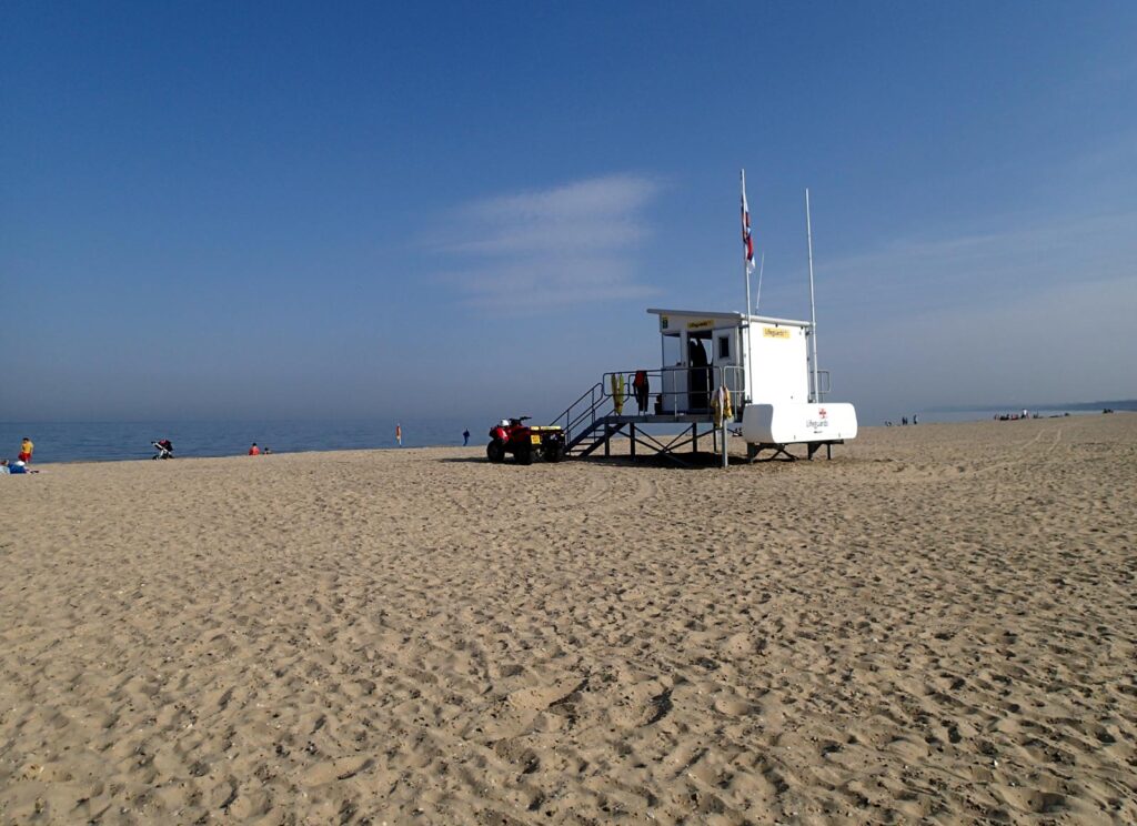 wide sandy beach, blue sky and sea, white temporary structure, the lifeguard station, in the centre
