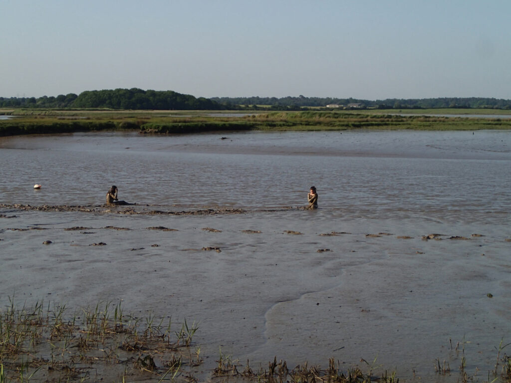 two children rolling in the mud , view across tidal river and marsh