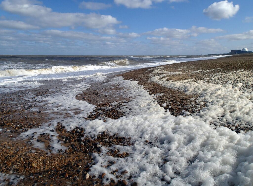 waves on a shingle beach, blue sky, distant view of power station