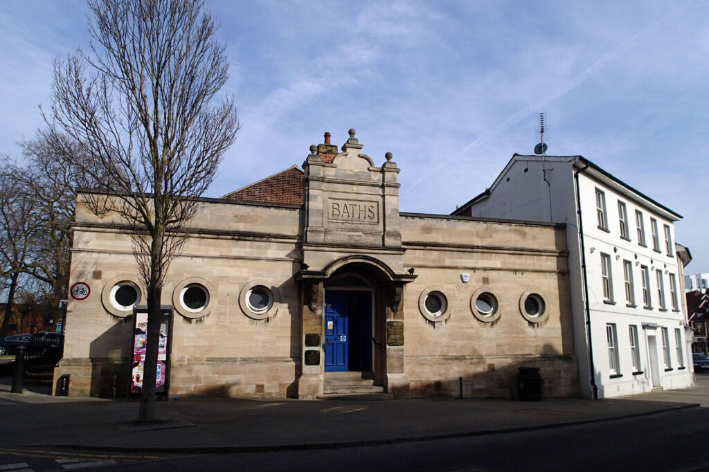 Low stone building with round windows, the word “BATHS” above entrance