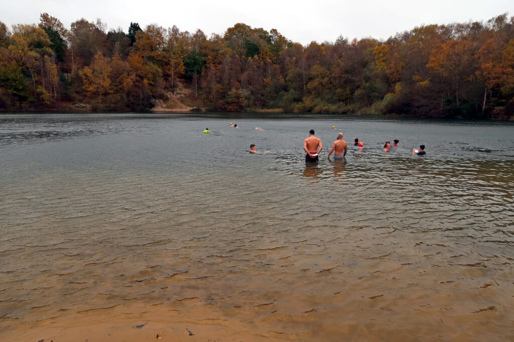 People swimming and standing in a lake with a wooded backdrop