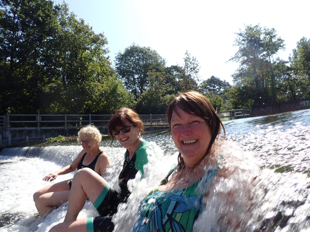 women in swim suits sitting on a weir with bubbling water, laughing