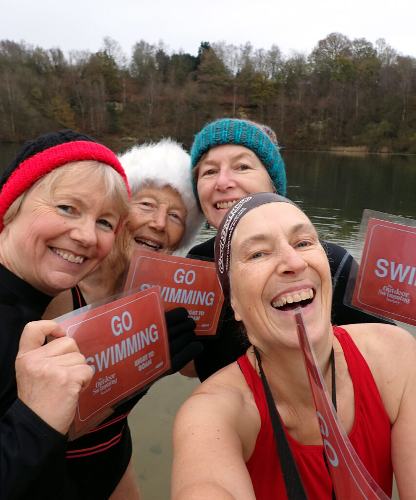 Four swimmers in a selfie with placards saying “Go Swimming”