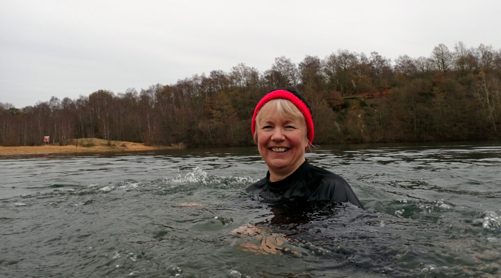 swimmer smiling with jolly red hat in a lake with a wooded backdrop