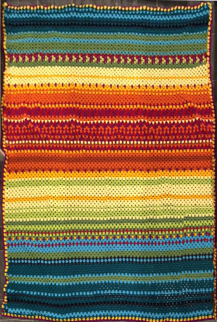 Blanket in stripes ranging from black to red through yellow green to blue