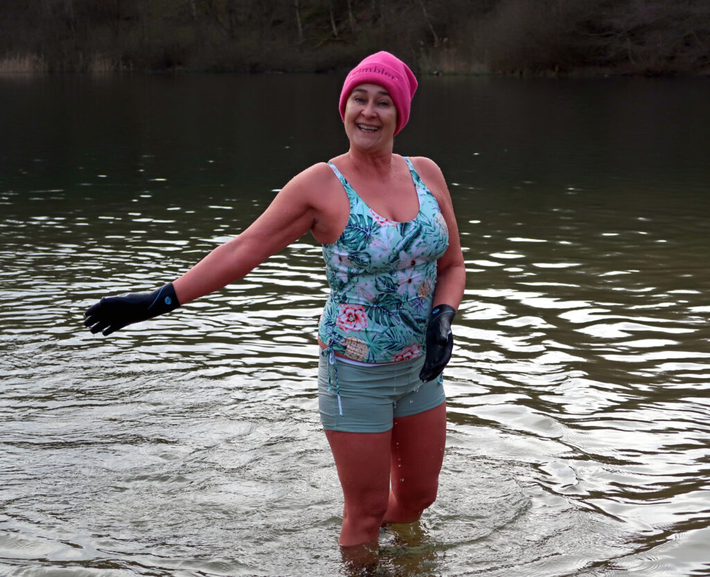 swimmer smiling in a lake in a colourful costume and neoprene gloves