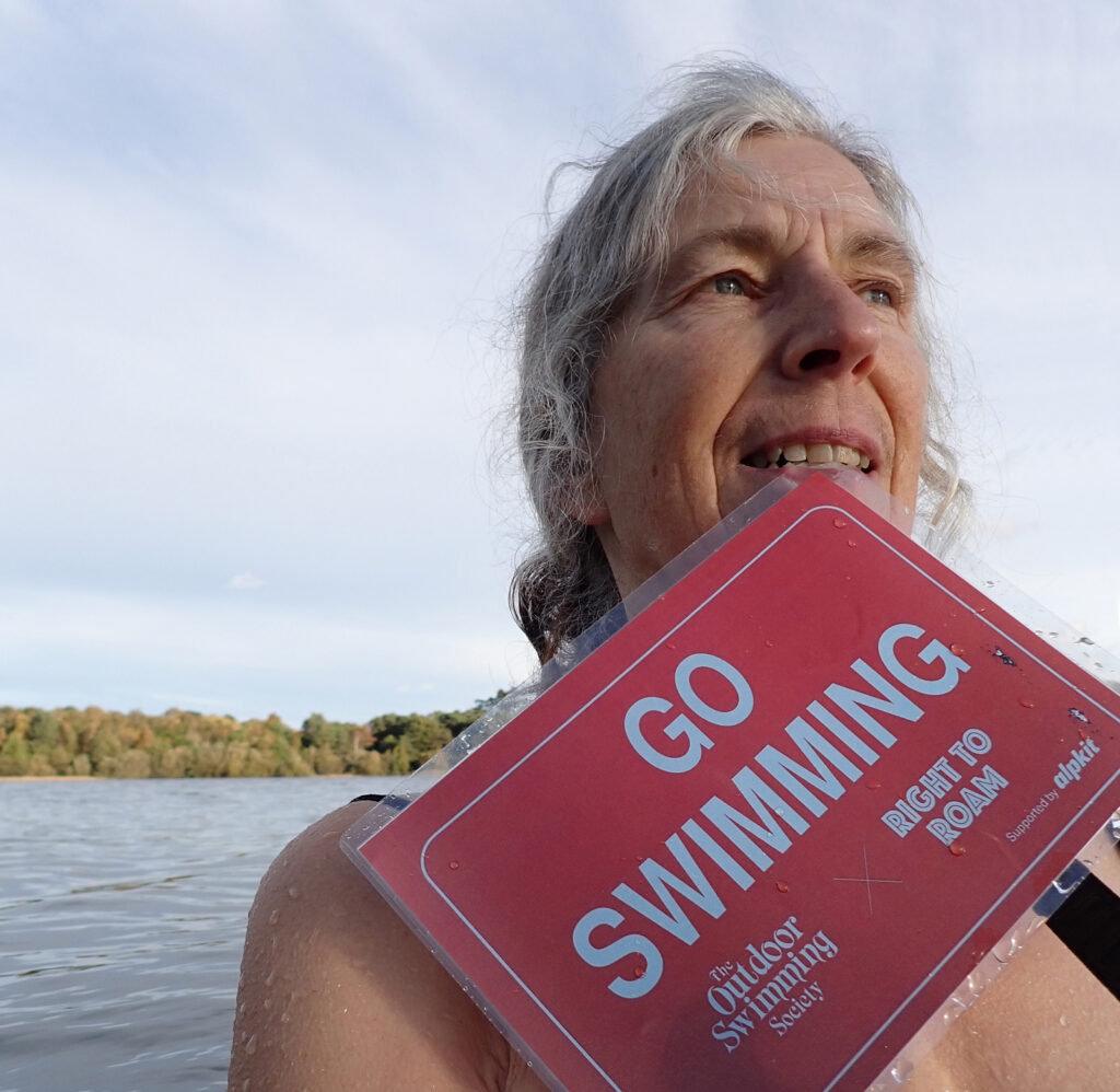 swimmer holding placard “Go Swimming” with blue sky and water behind
