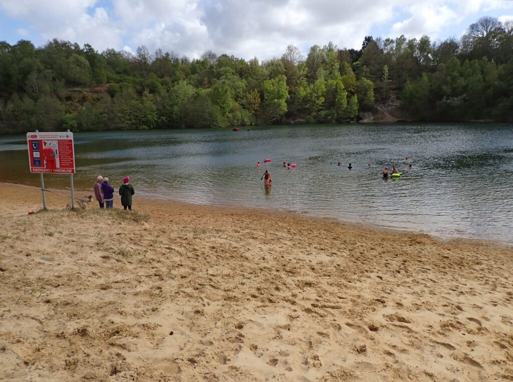 swimmers in the water at Brickyard Lake and three on shore, cliff rising behind the water