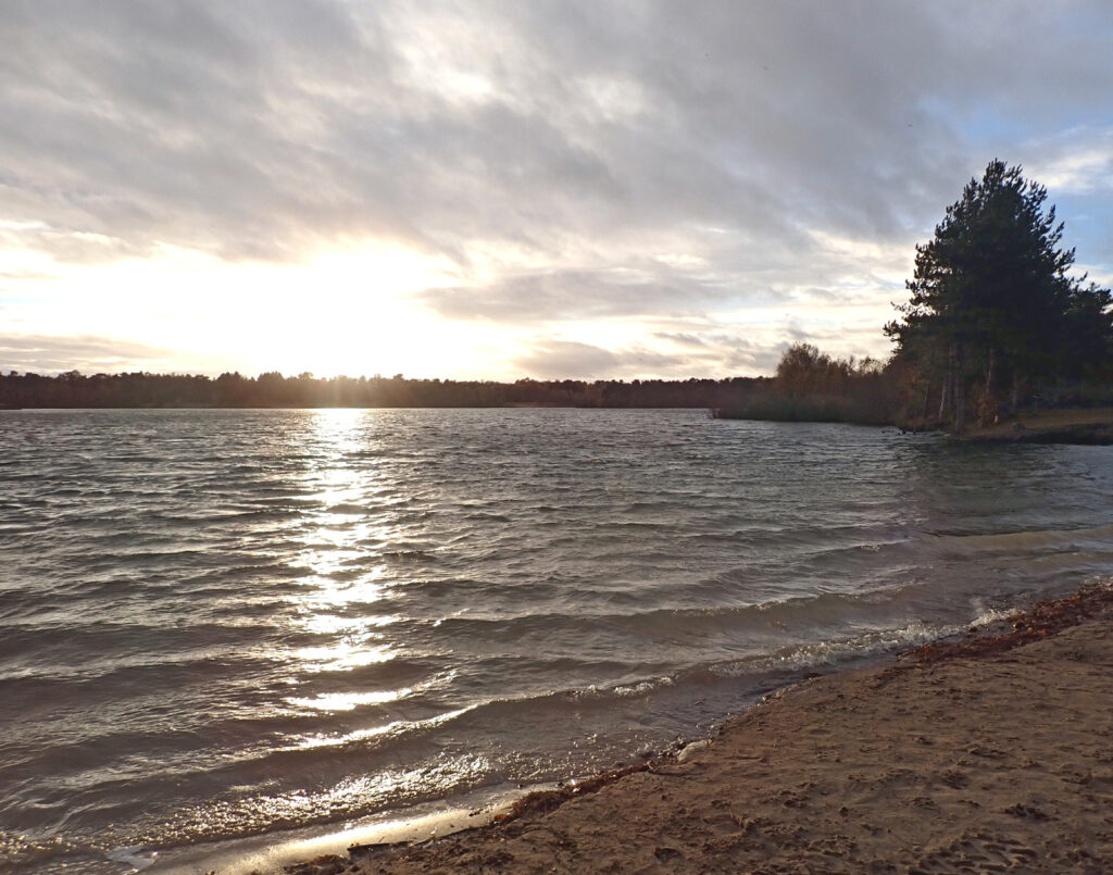 Great Lake, Bawsey Bay, gently rippling water and a sandy beach with setting sun shining across the water